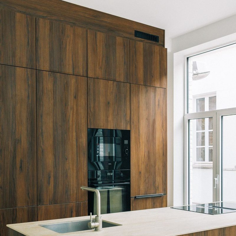 Walnut cabinet wall to the ceiling with two built-in ovens, beside a tall window