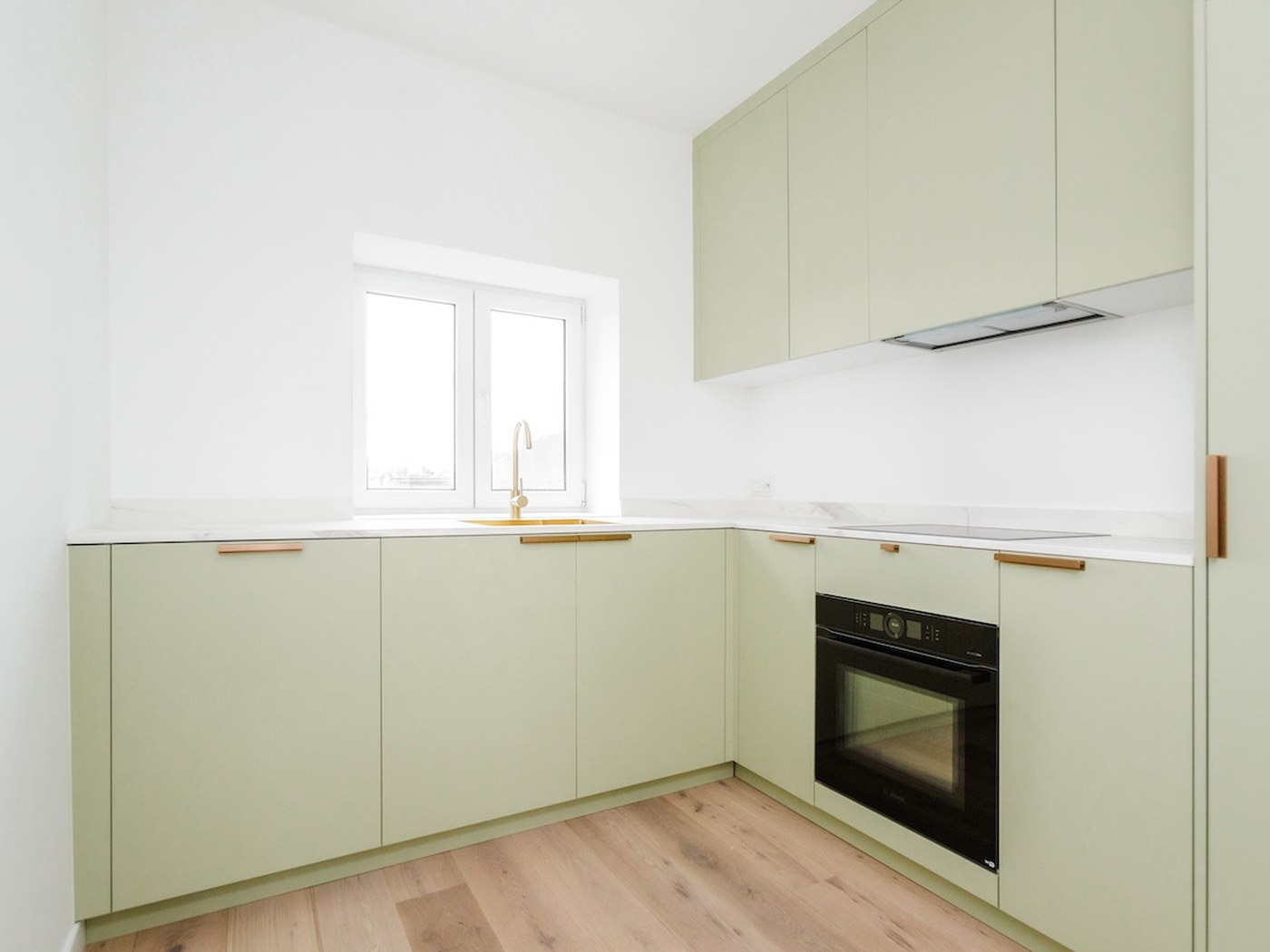 Saliegroene hoekkeuken met een ingebouwde oven op een lichte houten vloer
