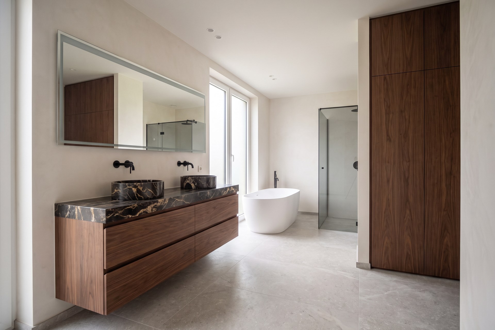 Design of a bathroom with a floating walnut vanity unit, a wide mirror, a freestanding bath and a tall walnut cabinet