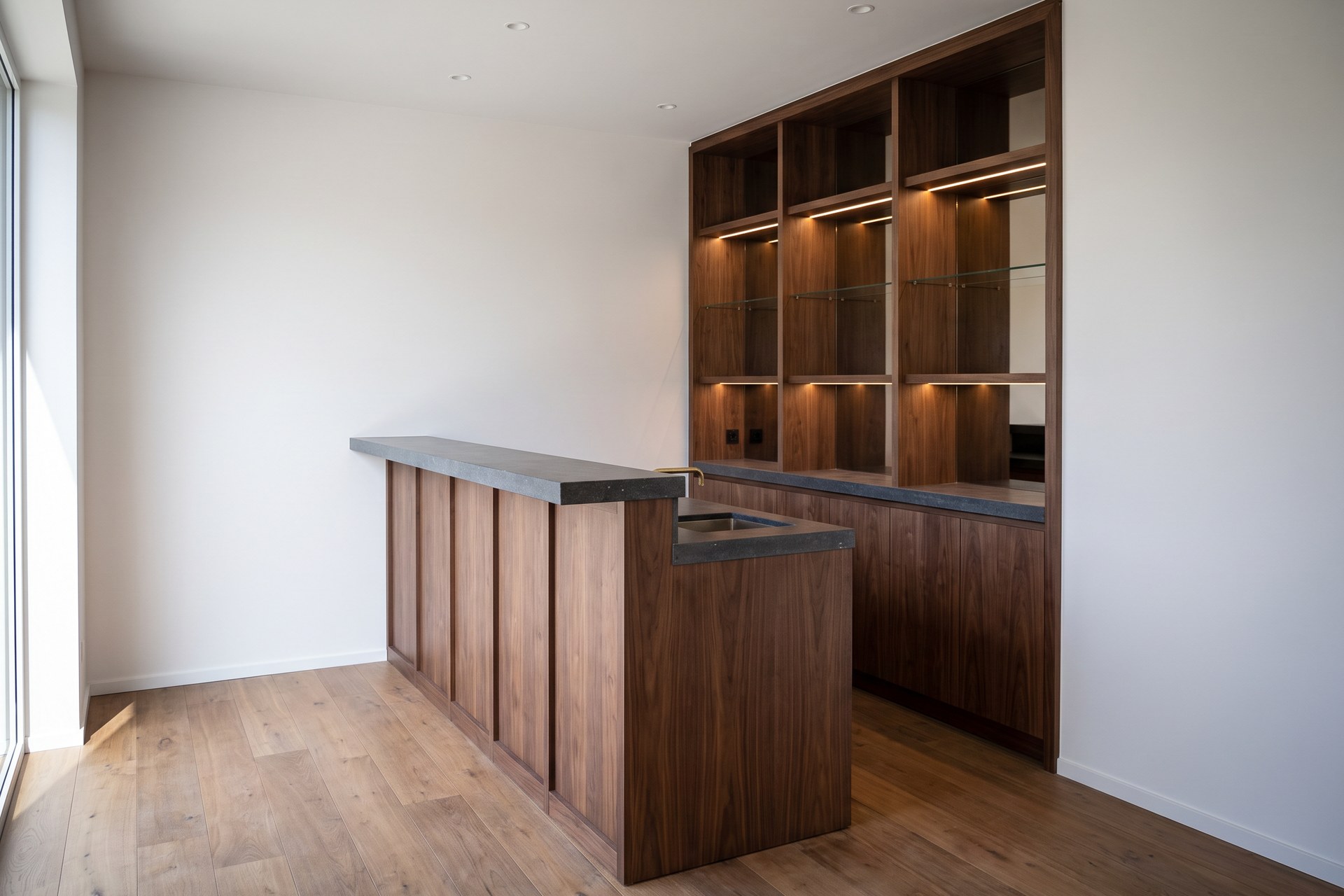 Ontwerp van een bar in notelaar met een toog in hardsteen en verlichte nissen
