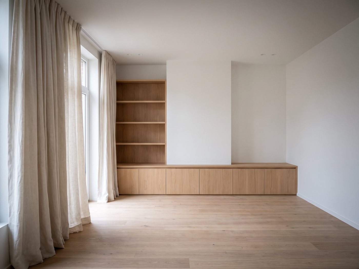 Design of a living space with a bookcase and a low cabinet in oak, and linen curtains at the windows